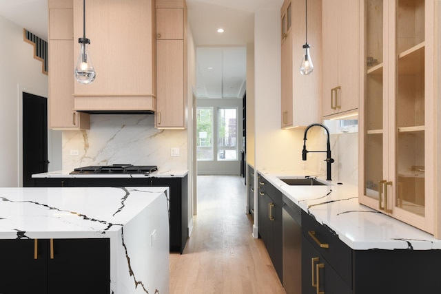 kitchen with light stone counters, sink, pendant lighting, and light hardwood / wood-style floors