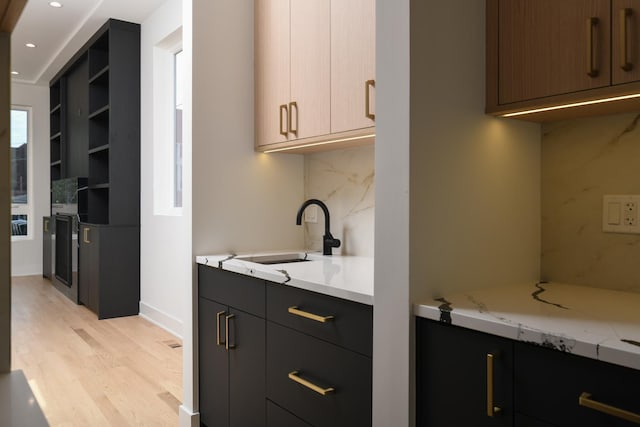 kitchen featuring light stone countertops, tasteful backsplash, light hardwood / wood-style floors, and sink