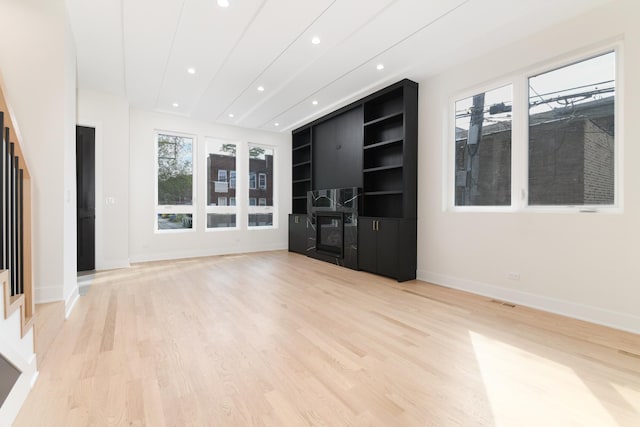 unfurnished living room with built in shelves, a fireplace, and light wood-type flooring