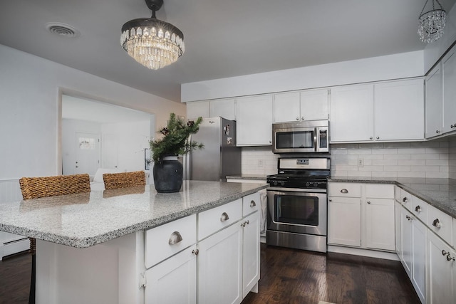 kitchen with tasteful backsplash, white cabinetry, stainless steel appliances, and decorative light fixtures