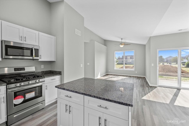 kitchen with white cabinets, stainless steel appliances, vaulted ceiling, and dark stone counters