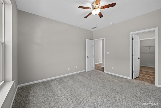 unfurnished bedroom featuring a closet, a walk in closet, carpet floors, and ceiling fan