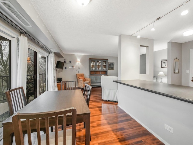 dining space with wood-type flooring, a textured ceiling, and track lighting