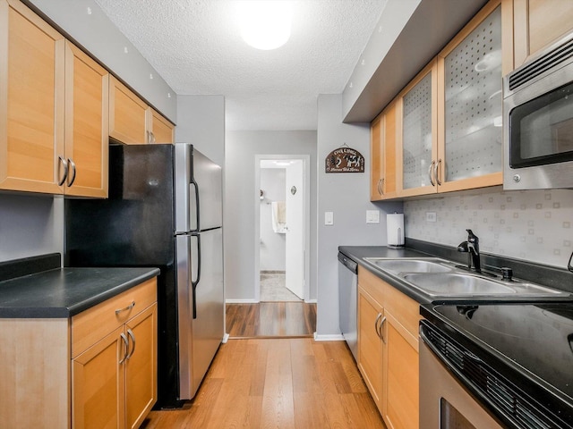 kitchen with backsplash, sink, a textured ceiling, light hardwood / wood-style floors, and stainless steel appliances