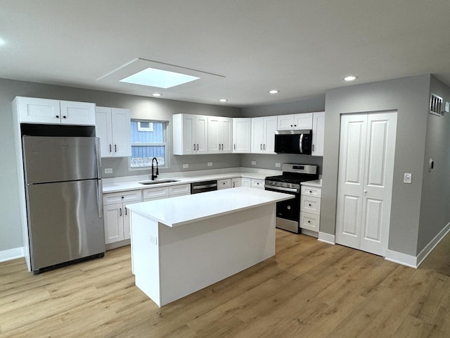 kitchen featuring a skylight, stainless steel appliances, a kitchen island, sink, and white cabinetry