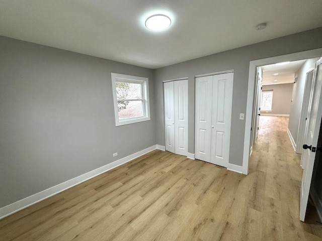 unfurnished bedroom with light wood-type flooring, multiple closets, and multiple windows