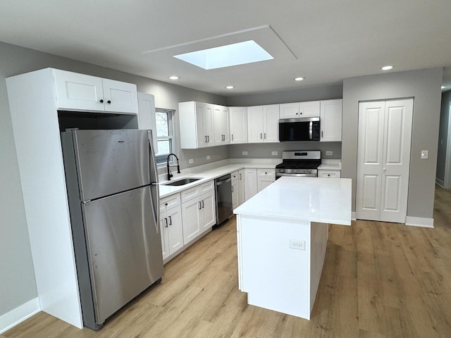 kitchen featuring a skylight, white cabinetry, sink, a center island, and appliances with stainless steel finishes