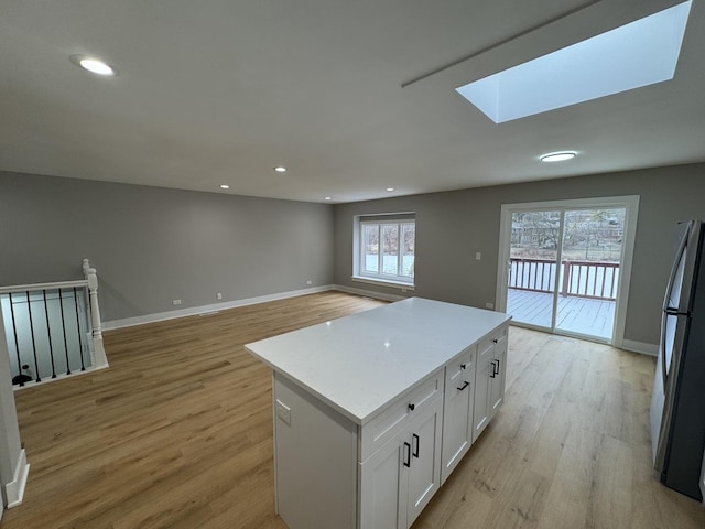 kitchen with a center island, white cabinets, light hardwood / wood-style flooring, a skylight, and stainless steel fridge