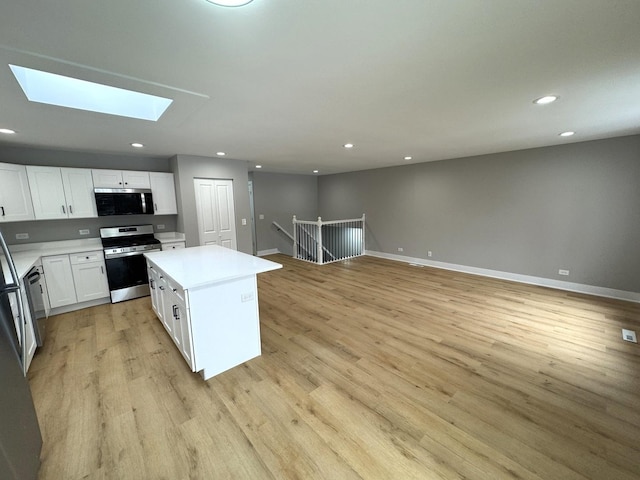 kitchen featuring a skylight, a center island, light hardwood / wood-style floors, white cabinets, and appliances with stainless steel finishes