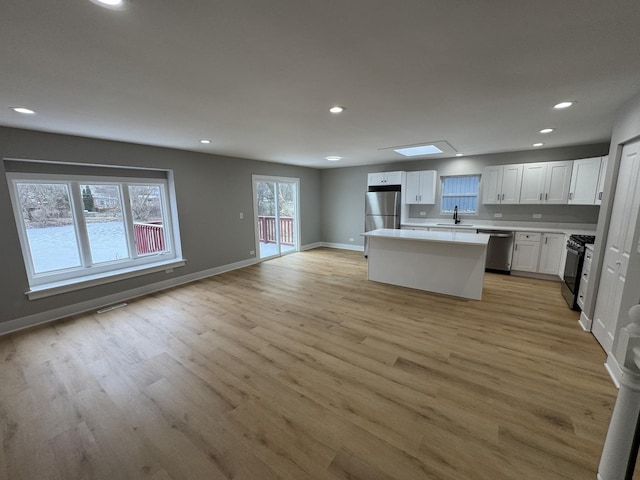 kitchen featuring a skylight, a kitchen island, appliances with stainless steel finishes, light hardwood / wood-style floors, and white cabinetry