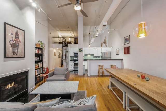 living room featuring light wood-type flooring, a towering ceiling, rail lighting, and ceiling fan