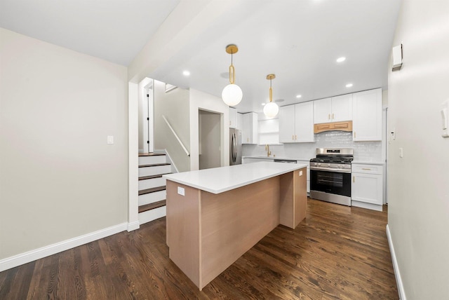 kitchen with appliances with stainless steel finishes, dark hardwood / wood-style flooring, pendant lighting, white cabinetry, and a kitchen island