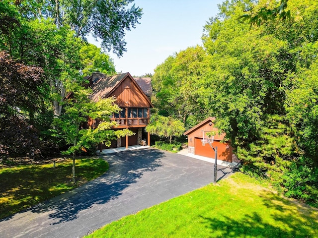 view of front facade featuring aphalt driveway, a front yard, an attached garage, and an outbuilding