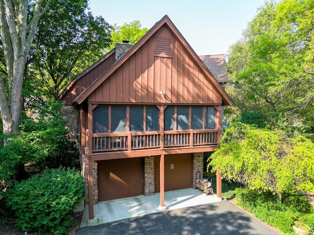 view of front of property featuring a patio, aphalt driveway, a sunroom, stone siding, and a chimney