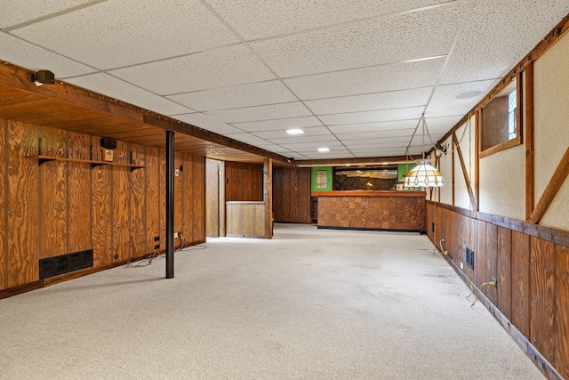 basement with light carpet, a paneled ceiling, and wood walls