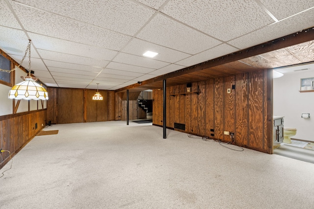 basement with a drop ceiling, light colored carpet, and wooden walls