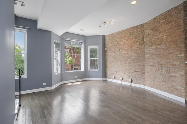 empty room featuring plenty of natural light, dark wood-type flooring, and brick wall