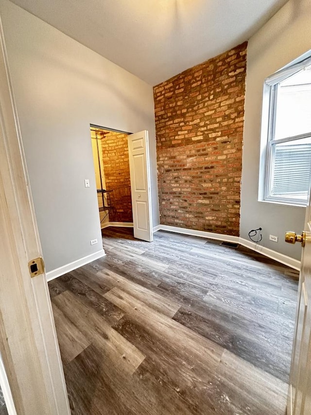 spare room with dark hardwood / wood-style flooring and brick wall