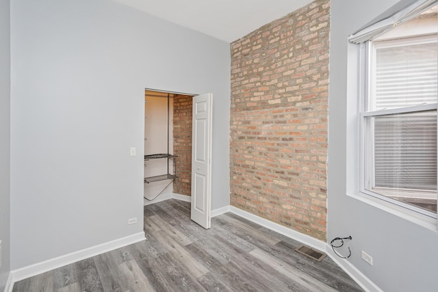 spare room with brick wall and light wood-type flooring