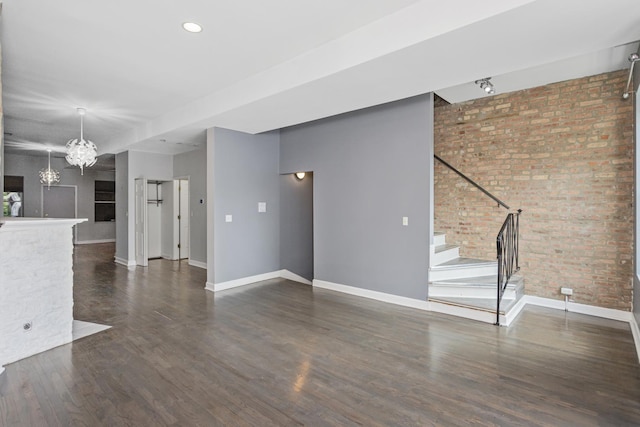 unfurnished living room featuring dark hardwood / wood-style flooring, brick wall, and a notable chandelier