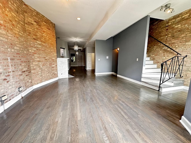 unfurnished living room featuring a chandelier, dark hardwood / wood-style flooring, and brick wall