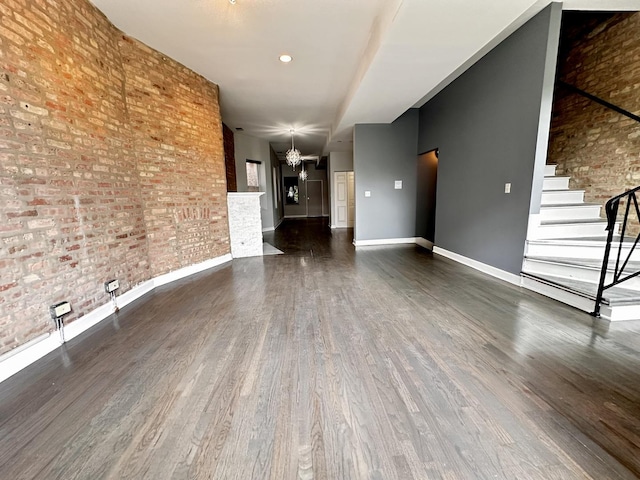 unfurnished living room featuring a notable chandelier, dark wood-type flooring, and brick wall