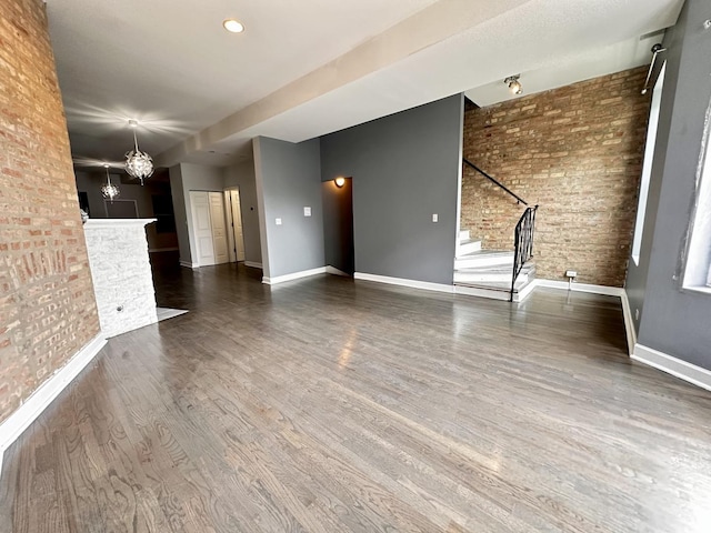 unfurnished living room featuring dark hardwood / wood-style floors, an inviting chandelier, and brick wall