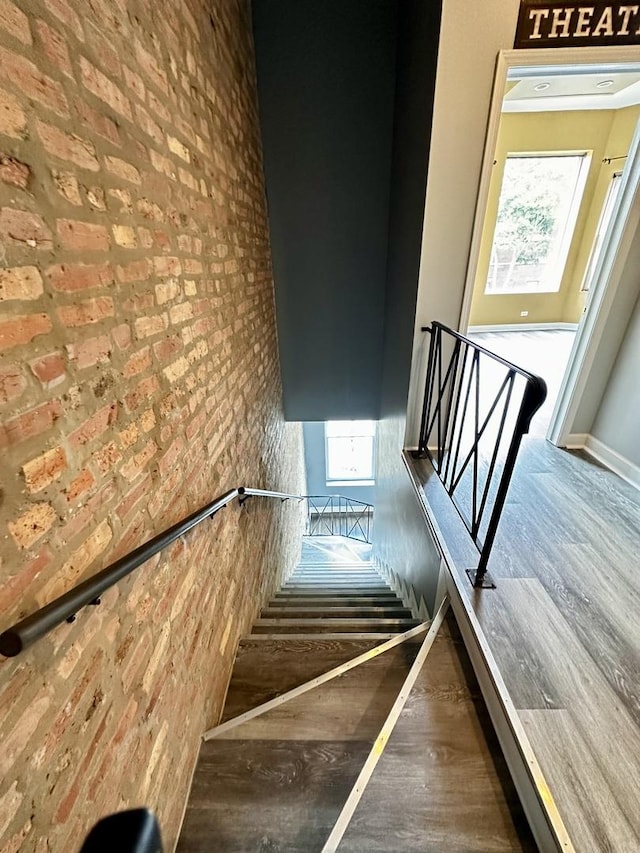 stairs with a wealth of natural light, hardwood / wood-style floors, and brick wall