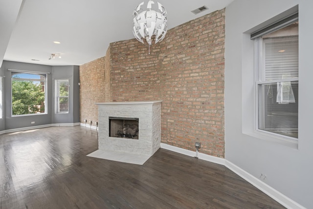 unfurnished living room with hardwood / wood-style flooring, a stone fireplace, brick wall, and a chandelier