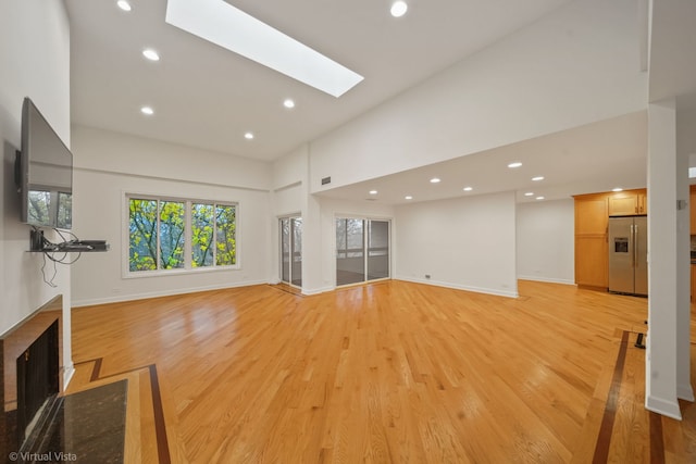 unfurnished living room featuring a skylight, a high ceiling, and light wood-type flooring