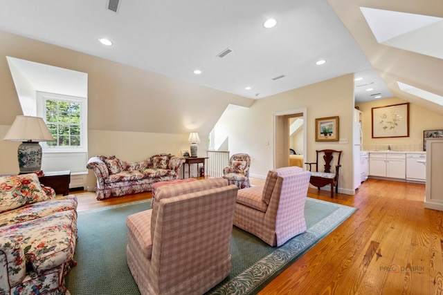 living room with vaulted ceiling with skylight and light hardwood / wood-style floors