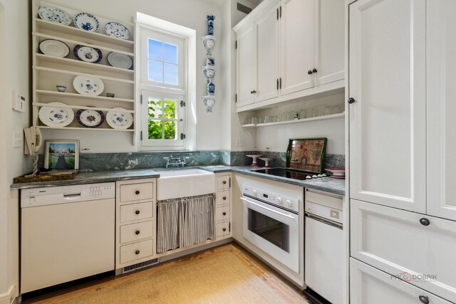 kitchen with white cabinetry, sink, dark stone countertops, white appliances, and light hardwood / wood-style flooring