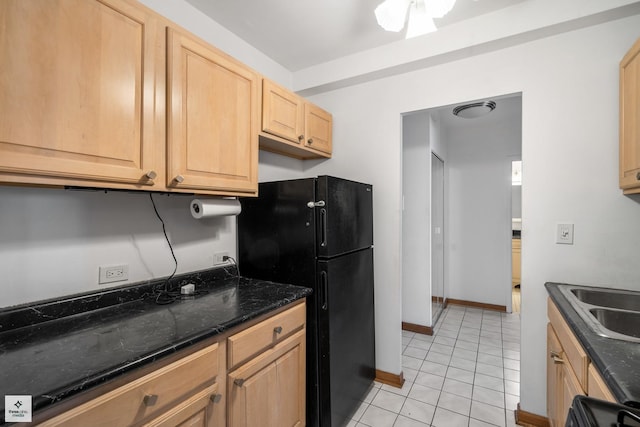 kitchen featuring sink, black fridge, dark stone countertops, light brown cabinetry, and light tile patterned floors