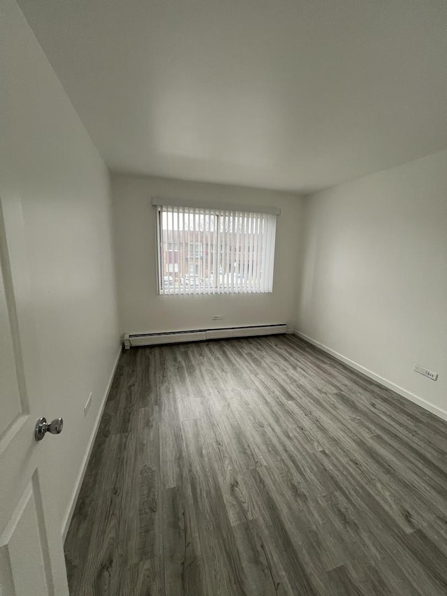 empty room with dark wood-type flooring and a baseboard heating unit