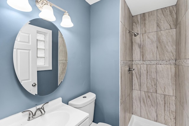 bathroom featuring toilet, tiled shower, and sink