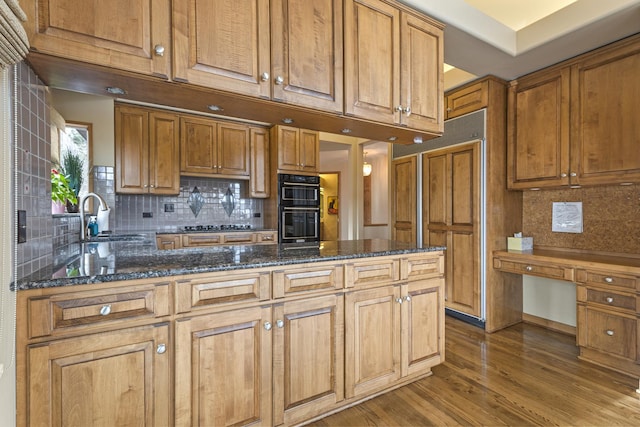 kitchen with double oven, sink, dark stone counters, and wood-type flooring