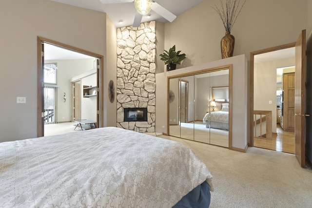 carpeted bedroom with ceiling fan, a fireplace, a high ceiling, and a closet