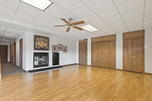 unfurnished living room featuring light wood-type flooring, ceiling fan, and a tiled fireplace