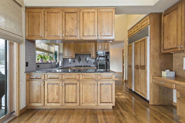 kitchen with sink, paneled fridge, dark hardwood / wood-style flooring, double oven, and dark stone counters