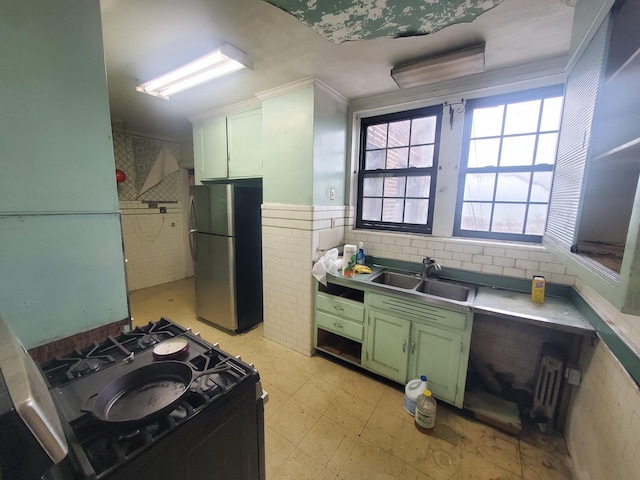 kitchen featuring green cabinetry, sink, black range with gas stovetop, and stainless steel refrigerator