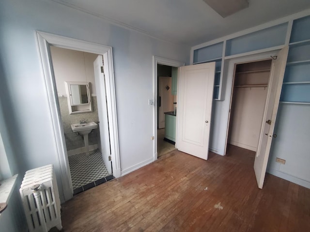 unfurnished bedroom with dark hardwood / wood-style flooring, ensuite bathroom, radiator heating unit, and a closet