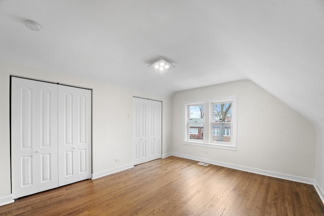 unfurnished bedroom with vaulted ceiling, hardwood / wood-style floors, and two closets