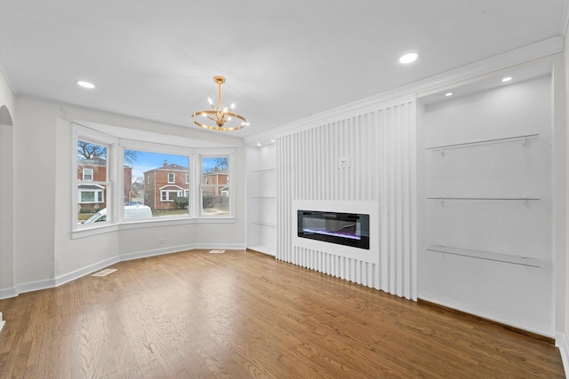 unfurnished living room featuring hardwood / wood-style floors, crown molding, a large fireplace, and a chandelier