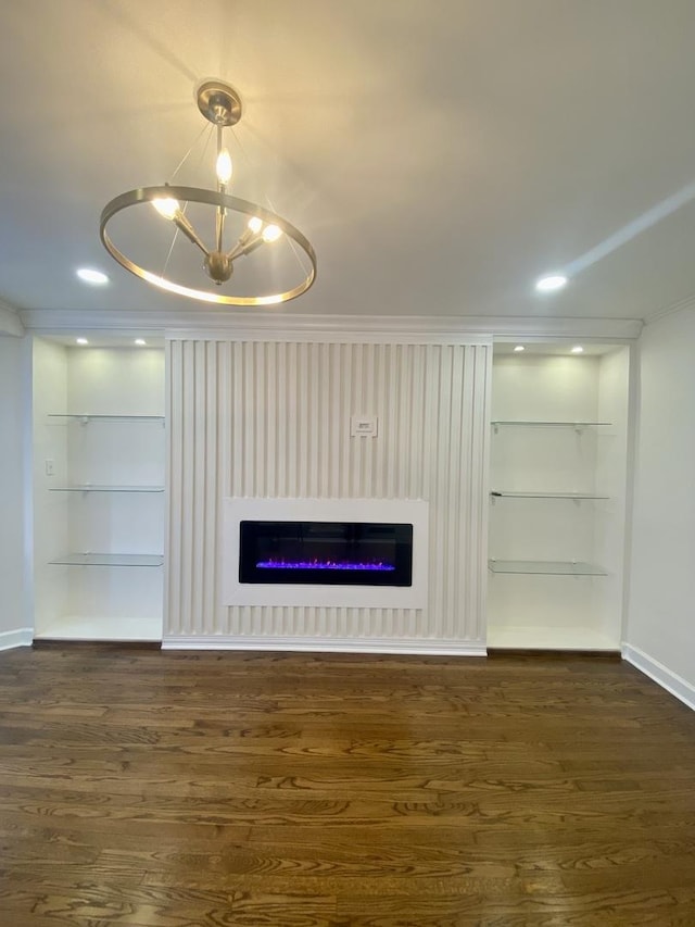 unfurnished living room with built in features, crown molding, dark wood-type flooring, and an inviting chandelier