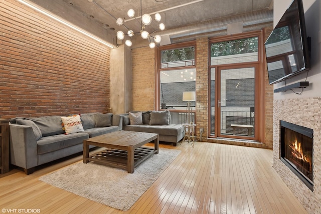 living room with a notable chandelier, brick wall, a high ceiling, and light wood-type flooring