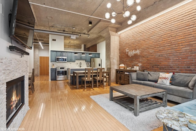 living room with a high ceiling, light hardwood / wood-style flooring, a stone fireplace, and brick wall