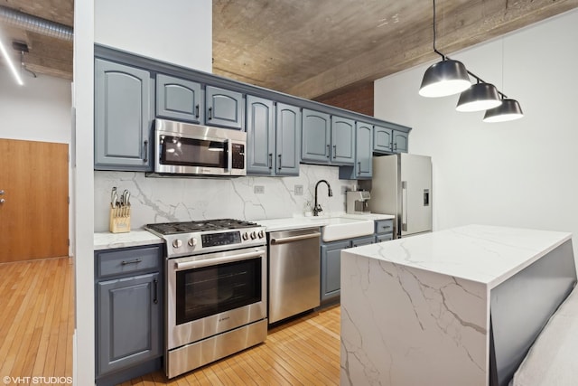 kitchen with pendant lighting, backsplash, sink, light stone countertops, and appliances with stainless steel finishes