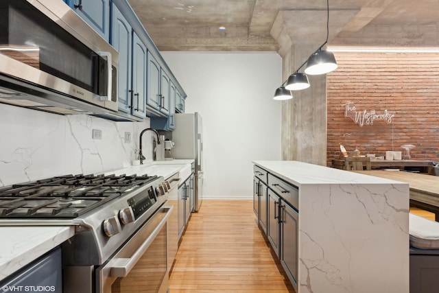 kitchen with light stone countertops, appliances with stainless steel finishes, blue cabinets, light hardwood / wood-style floors, and hanging light fixtures