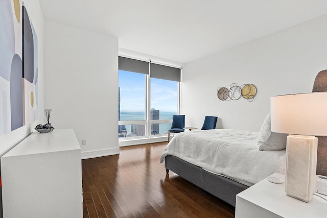 bedroom with dark hardwood / wood-style flooring, a wall of windows, and a water view