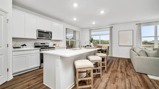 kitchen with sink, dark wood-type flooring, stainless steel appliances, a center island with sink, and white cabinets